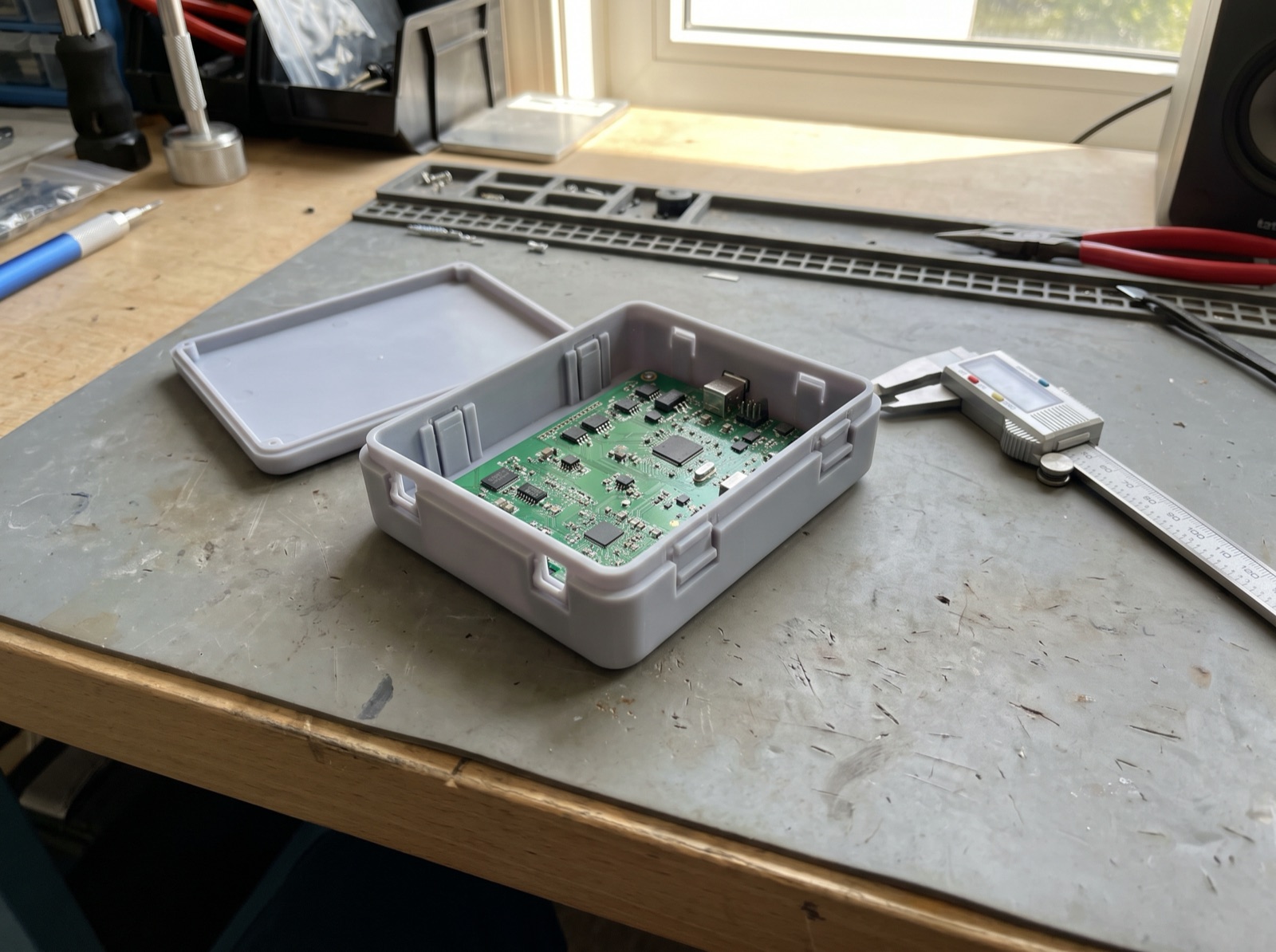 Gri reçineden basılmış, içinde elektronik kart bulunan geçme kapaklı muhafaza prototipi ve kumpas